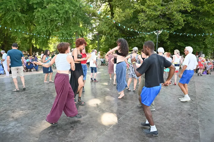 Danseurs de tous âges sur l'esplanade en plein air du Pâquier, sous les guirlandes lumineuses tendues entre les arbres