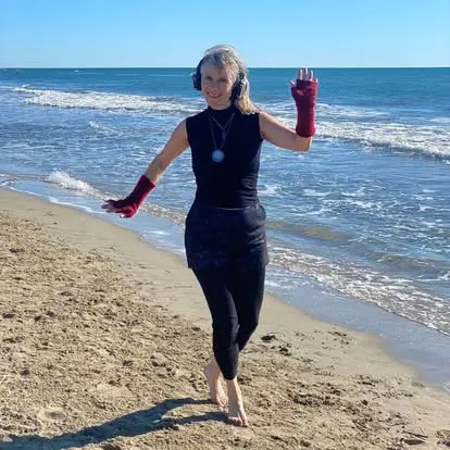 Photo d'une danseuse pieds nus marchant sur une plage au bord de la mer, casque audio sur les oreilles et mitaines rouges aux mains.